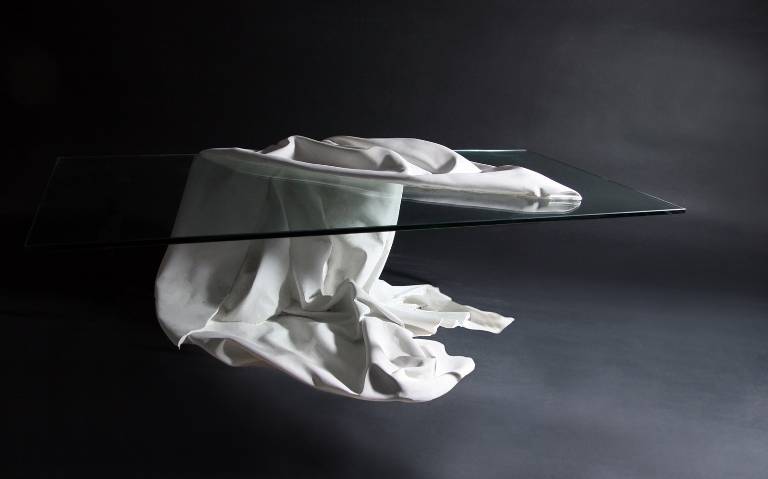 A coffee table that looks like a slab of glass is held up by a floating piece of cloth